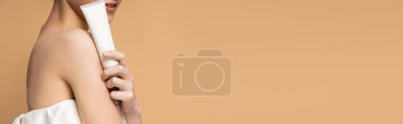 Cropped view of smiling woman with naked shoulder holding cosmetic balm isolated on beige, banner