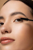Close up view of asian woman with natural visage posing near mascara applicator isolated on beige mug #666744656