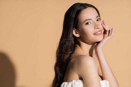 Beautiful asian woman in top smiling and looking at camera on beige background with shadow