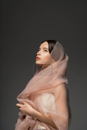 Hübsches junges asiatisches Model mit alltäglichem Make-up und beigem Tuch posiert isoliert auf grau