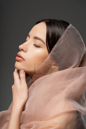 Porträt einer attraktiven jungen asiatischen Frau mit beigem Tuch posiert mit geschlossenen Augen isoliert auf beige