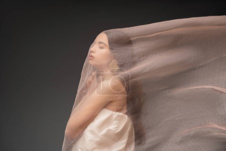 Téléchargez les photos : Jeune femme asiatique en haut avec épaule nue debout sous tissu isolé sur noir - en image libre de droit