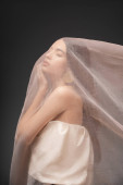 Young asian woman in top touching cheek while posing under beige cloth isolated on grey mug #666745778