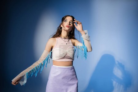 Fashionable young asian woman in skirt and mesh top posing on blue background with shadow