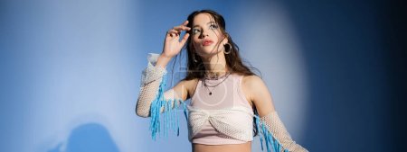 Trendy young asian model with bold makeup posing in mesh top on blue background with shadow, banner