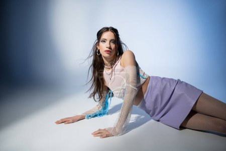 Trendy young asian woman in mesh top and skirt looking at camera while posing on blue background