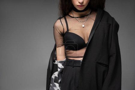 Cropped view of fashionable young model in sheer top and black jacket posing isolated on grey