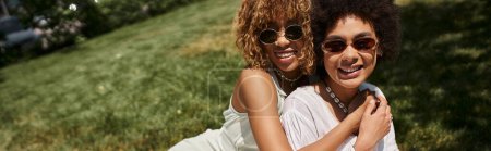 Téléchargez les photos : Pique-nique d'été, gaies femmes afro-américaines en robes blanches assises sur la pelouse verte, bannière - en image libre de droit