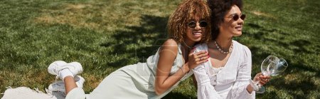 freudige afrikanisch-amerikanische Frau mit Sonnenbrille umarmt Freundin beim Picknick, Banner