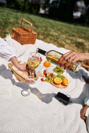 picnic de verano, vista parcial de la mujer afroamericana sosteniendo vidrio cerca de la novia vertiendo vino