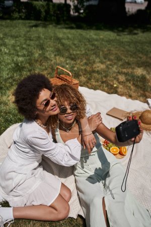 Foto de Africano americano mujer abrazando novia tomando selfie en vintage cámara, verano ocio - Imagen libre de derechos