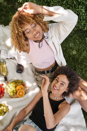 top view of african american woman smiling at camera near girlfriend with closed eyes, fun in park