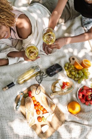 picnic de verano, vista superior de novias afroamericanas con copas de vino mirándose