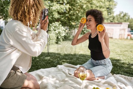 afro-américaine femme avec des moitiés d'orange près de petite amie avec caméra vintage et verre à vin