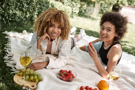 Sommerpicknick, positive afrikanisch-amerikanische Freundinnen blicken in die Kamera neben Obst und Weinglas