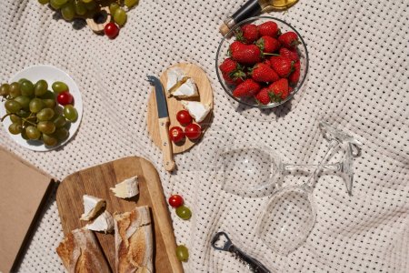 summer picnic concept, strawberries, grapes, cherry tomatoes, bread, cheese, wine glasses, top view