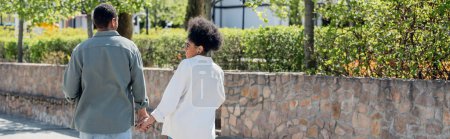 Téléchargez les photos : Femme afro-américaine gaie tenant la main du petit ami tout en marchant dans la rue urbaine, bannière - en image libre de droit