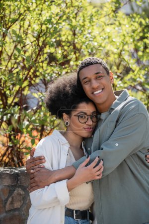 positive african american couple hugging while looking at camera together outdoors