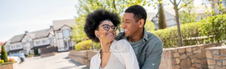 positive african american couple looking at each other on urban street in summer, banner