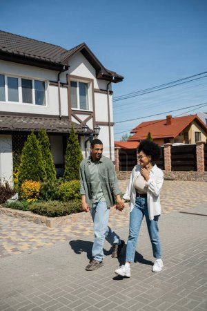 Photo for Positive romantic african american couple walking on sidewalk on urban street in summer - Royalty Free Image