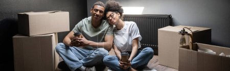 Téléchargez les photos : Heureux couple afro-américain tenant café à emporter près de boîtes en carton dans une nouvelle maison, bannière - en image libre de droit