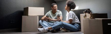 Téléchargez les photos : Couple afro-américain avec café à emporter parler près de boîtes en carton dans une nouvelle maison, bannière - en image libre de droit