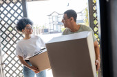 positive african american couple holding carton boxes near door of new house during moving tote bag #667987038