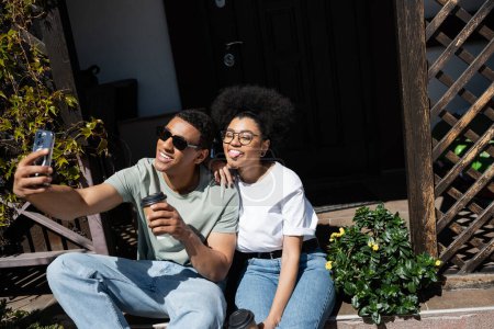 Afrikanisch-amerikanisches Paar mit Kaffee zu gehen Selfie auf Smartphone auf der Veranda des neuen Hauses