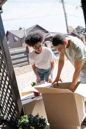 smiling african american couple unpacking cardboard boxes near new house outdoors
