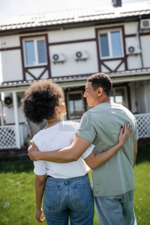 sonriente afroamericano hombre abrazando novia y hablando cerca de nueva casa borrosa