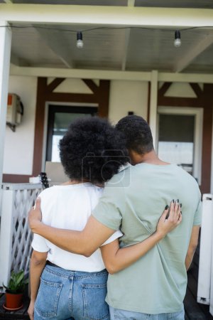 Rückansicht eines afrikanisch-amerikanischen Paares, das sich in der Nähe eines neuen Hauses im Freien umarmt