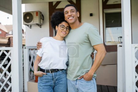positivo africano americano pareja abrazo y posando cerca borrosa nuevo casa en fondo