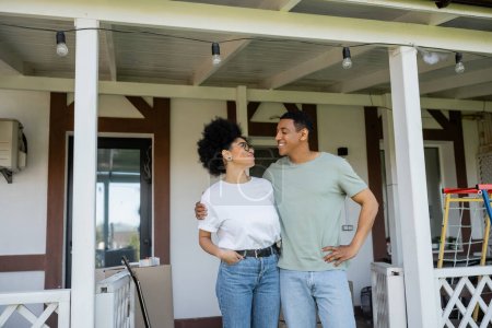feliz africano americano pareja abrazando mientras de pie en porche cerca de nueva casa al aire libre