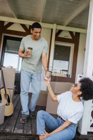 souriant homme afro-américain donnant du café pour aller à petite amie sur le porche de la nouvelle maison