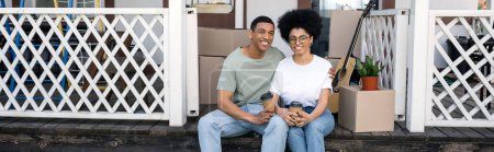 Foto de Pareja afroamericana positiva con café para llevar sentados juntos en el porche de un nuevo hogar, pancarta - Imagen libre de derechos