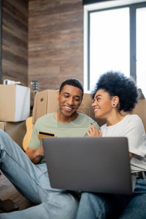 Téléchargez les photos : Heureux couple afro-américain faisant des achats en ligne près de paquets dans le salon à la maison - en image libre de droit