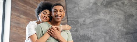 joyful african american woman hugging smiling boyfriend in new house, banner