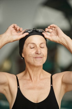 portrait, active lifestyle, mature woman in swimwear, adjusting goggles, swim cap, spa center