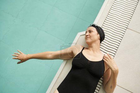cheerful middle aged woman lying at poolside, top view, swim cap and goggles, pool water, spa center