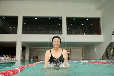Wasserspritzer, reife Frau mit Badekappe und Brille, die Spaß im Pool hat, geschlossene Augen, Wellness-Center