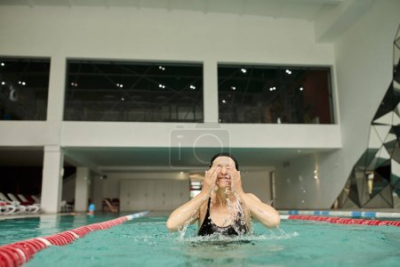 salpicaduras de agua, mujer de mediana edad en gorra de natación divirtiéndose en la piscina, ojos cerrados, centro de spa, dichoso