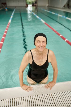 fröhliche Frau mittleren Alters in Badekappe und Brille am Pool, lächelnd, Erholungszentrum, Wellness