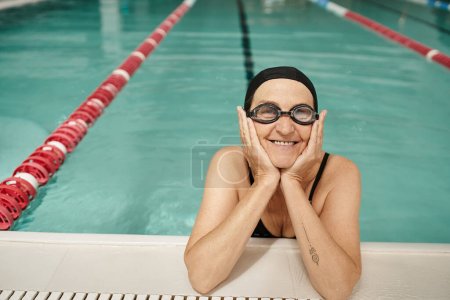 Photo for Happy middle aged woman in swim cap and goggles, swimming pool, recreation center, tattoo, poolside - Royalty Free Image