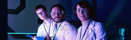 Foto de Pancarta, Tres científicos participan en el análisis de la cabeza dentro de Neon-Lit Science Center. - Imagen libre de derechos