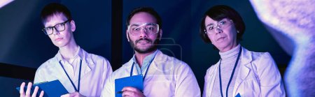 Téléchargez les photos : Bannière, Trois scientifiques examinent l'appareil nouvellement créé dans Neon-Lit Science Center - en image libre de droit