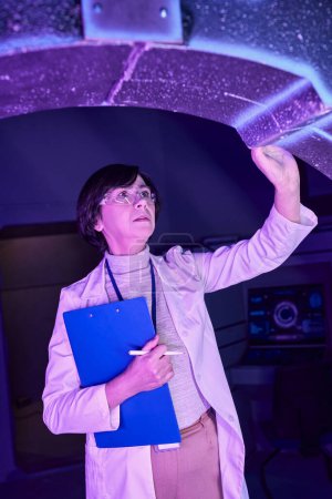 centro de ciencia futurista, científica femenina con portapapeles examinando dispositivo innovador