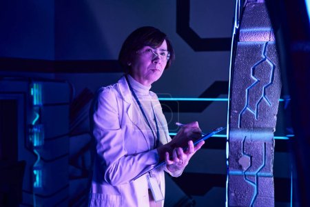 futuristisches Konzept, durchdachte Wissenschaftlerin schreibt auf Klemmbrett im neonbeleuchteten Entdeckungszentrum