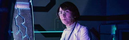 Wissenschaft der Zukunft, ernsthafte Wissenschaftlerin mittleren Alters in futuristischer neonbeleuchteter Technologiedrehscheibe, Banner