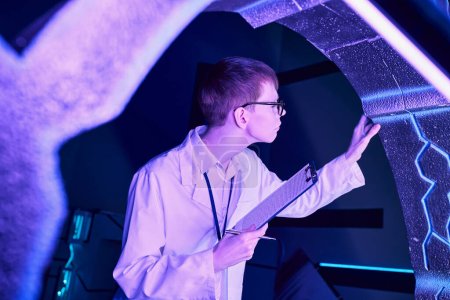 Foto de Tecnologías futuras, joven interno con portapapeles examinando nuevos equipos en el centro de ciencia - Imagen libre de derechos