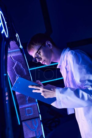 Junge Praktikantin schreibt auf Klemmbrett in der Nähe neuer Experimentiergeräte im Science Center der Zukunft